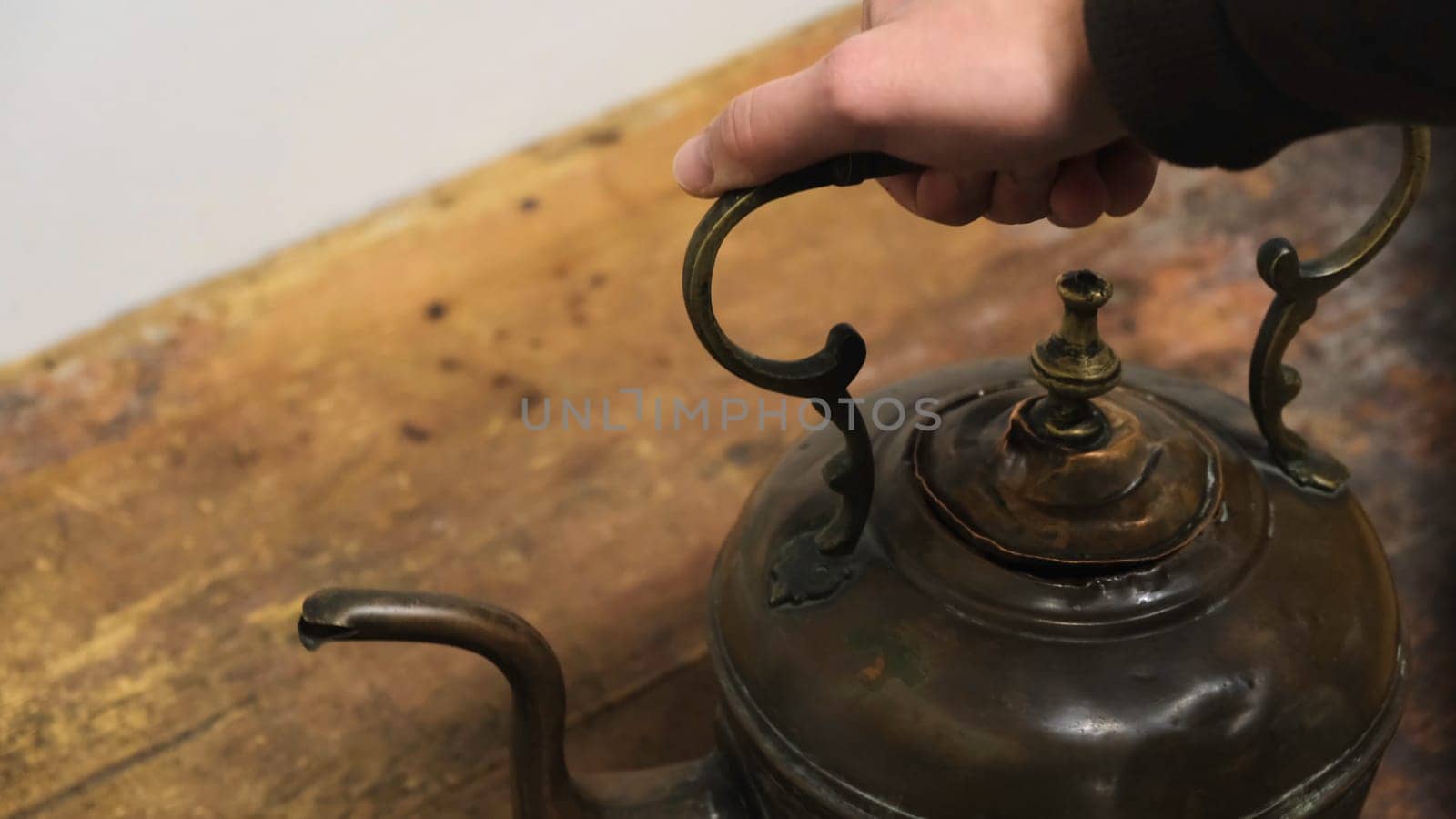 Close-up of man's hand taking an old iron kettle from the wooden board. Exposition at the Museum