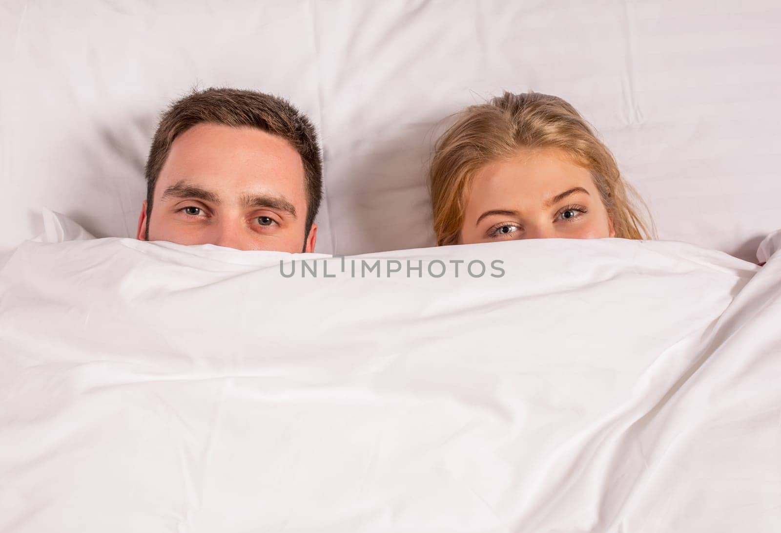 Young lovely couple lying in a bed, looking at camera, cover under blanket top angle view up above