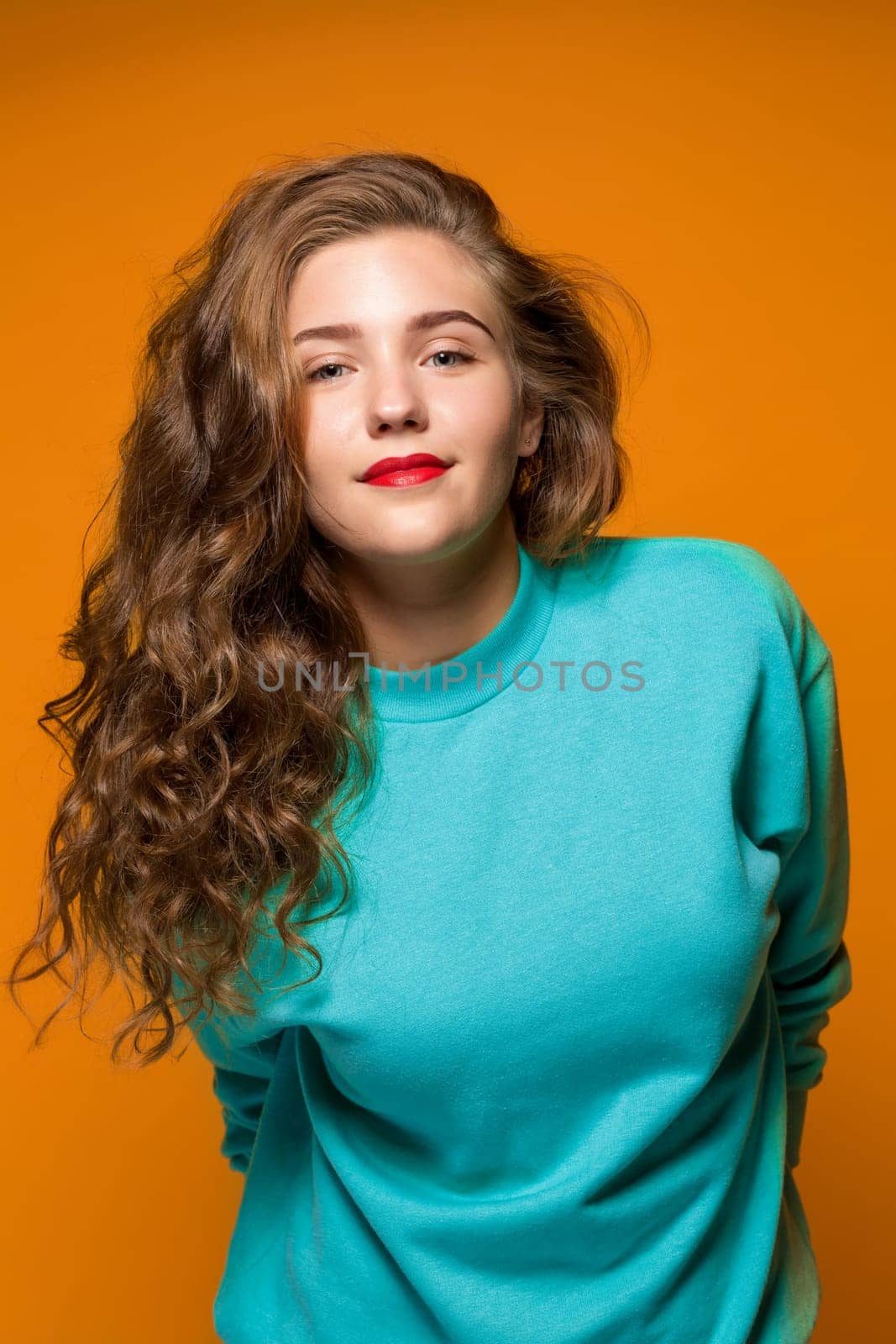 Portrait beautiful young brunette woman with wavy hair, looking at the camera, on orange background