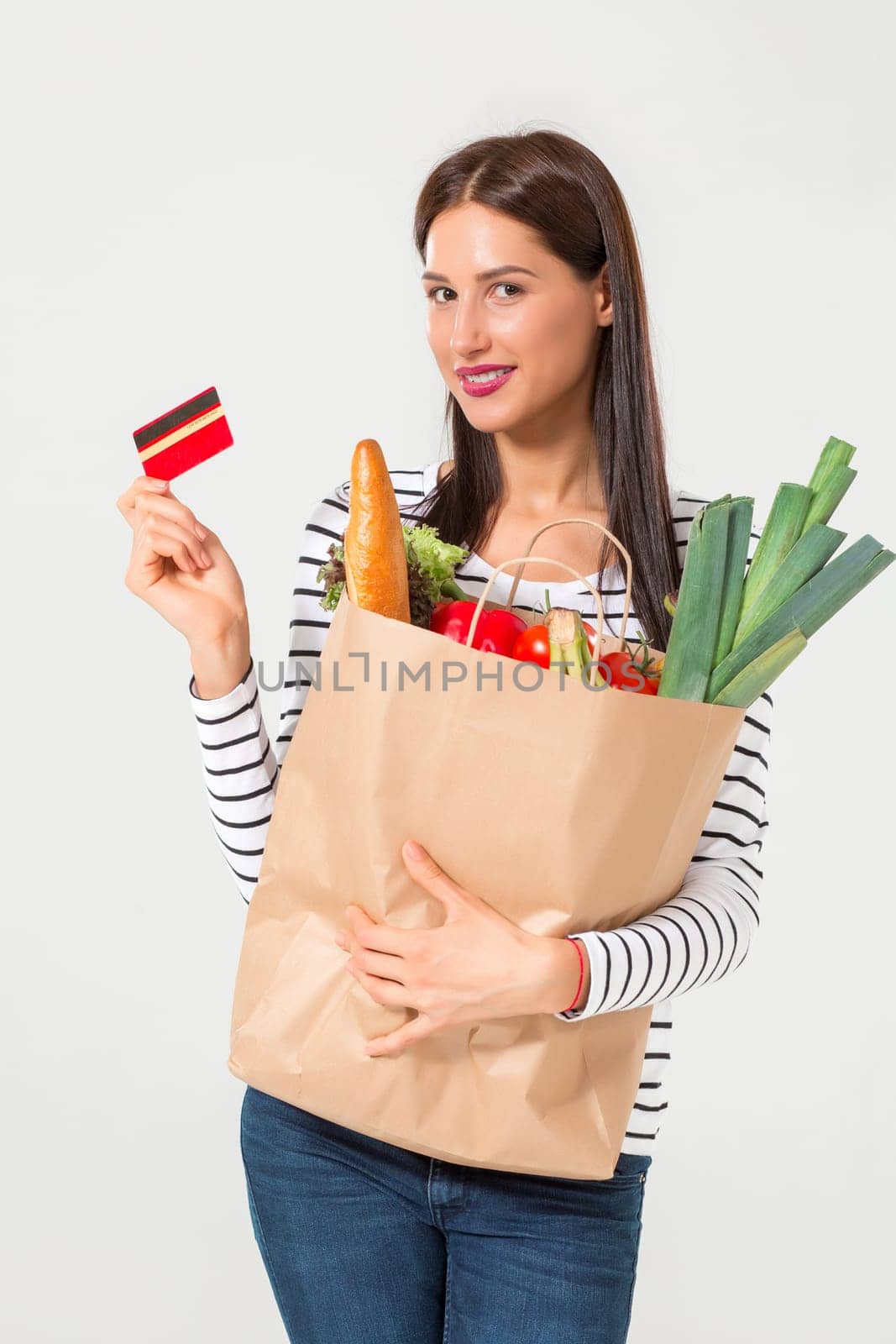 Beautiful young woman with credit card holding groceries in eco paper bag. Female consumer in shop. Concept of online shopping