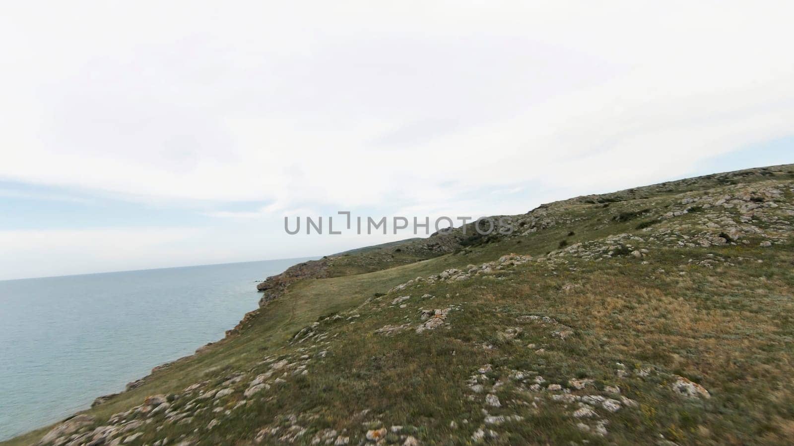 Aerial view of green hills and stones on cloudy sky and sea background. Shot. Flying above beautiful mountain top