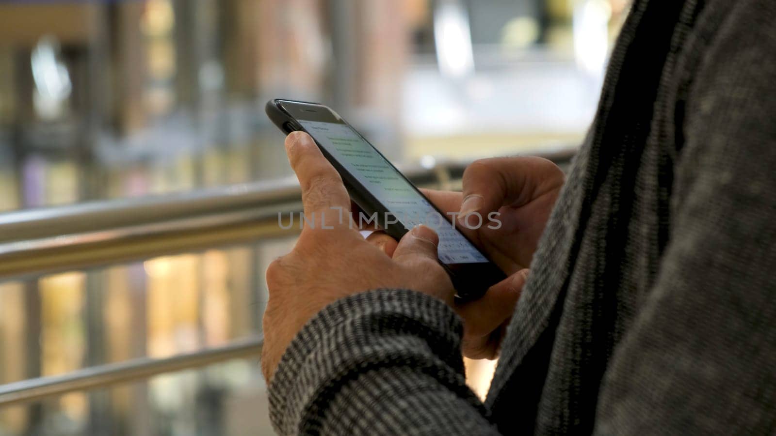 Close up of man hands texting a message on shopping mall background. Male hands using his smartphone for chatting in social net.