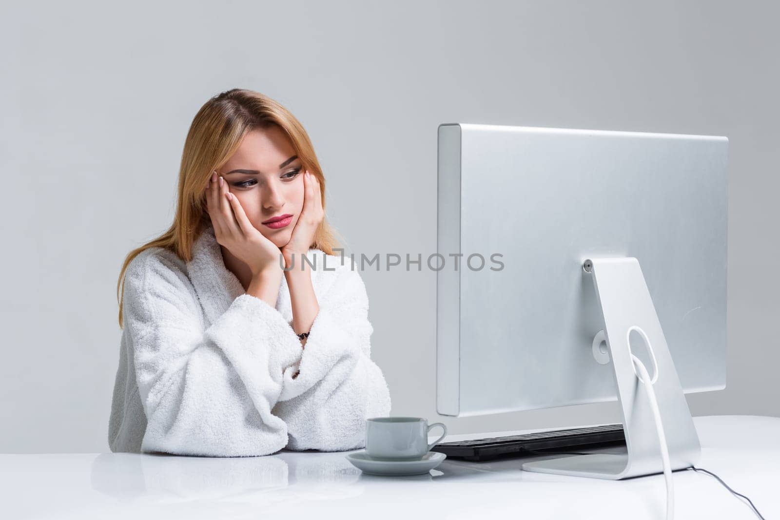 young woman sitting in the table and using computer on gray background. sleepy in the morning looking at the monitor