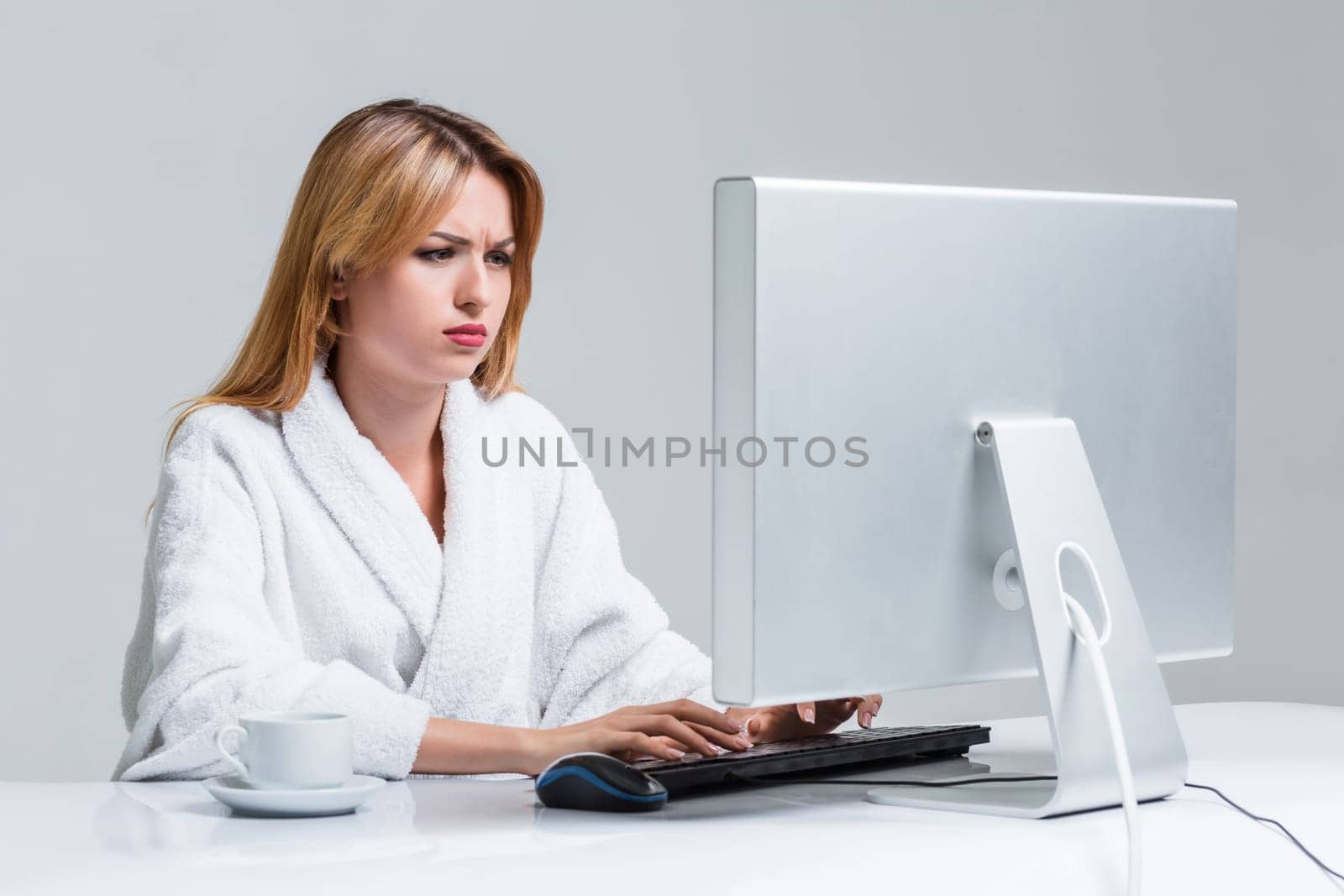 young woman sitting in the table and using computer on gray background. sleepy in the morning looking at the monitor