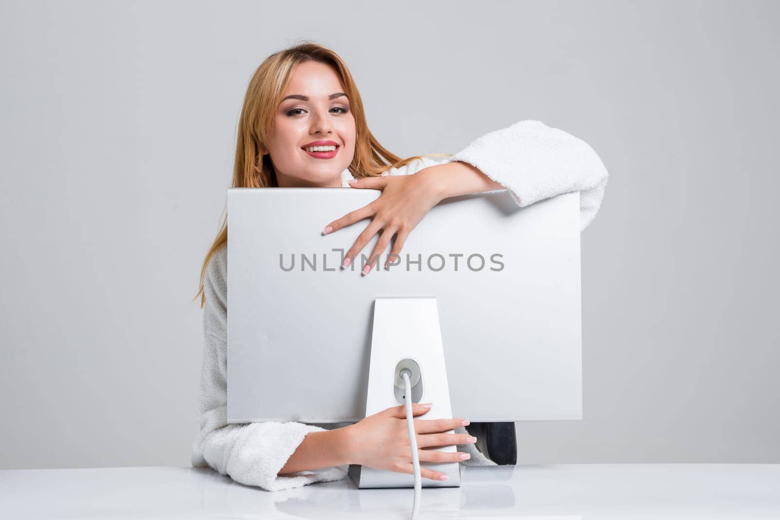 young woman sitting in the table and using computer on gray background. satisfied smiling girl hugging Monitor