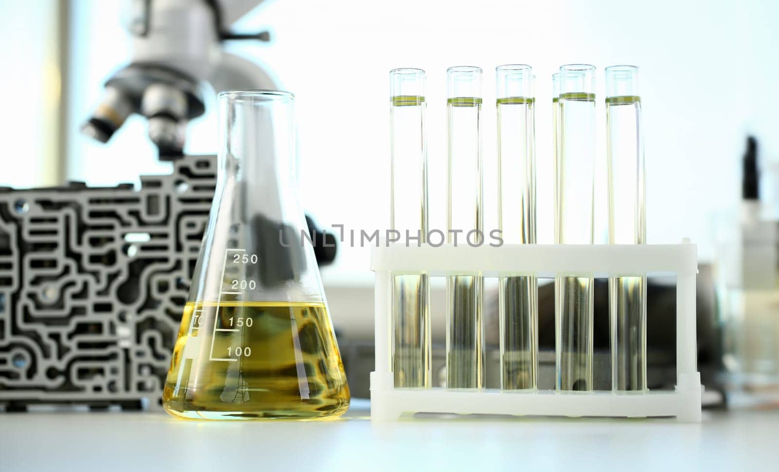 Test tube chemistry flask against background of hydroblock acp with yellow liquid purified oil from recycling and lubricating materials sale closeup