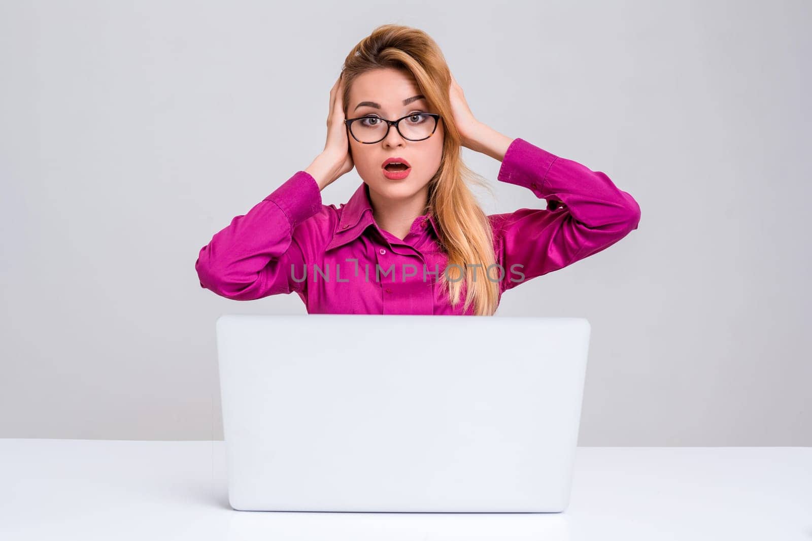 Young businesswoman working at laptop computer. she is going through and looking at the camera. her head in her hands
