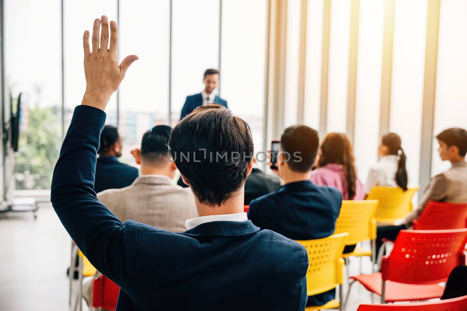 Curious individual in a diverse group raises a hand during a conference. This active participation showcases collaboration teamwork and engagement in discussions by Sorapop