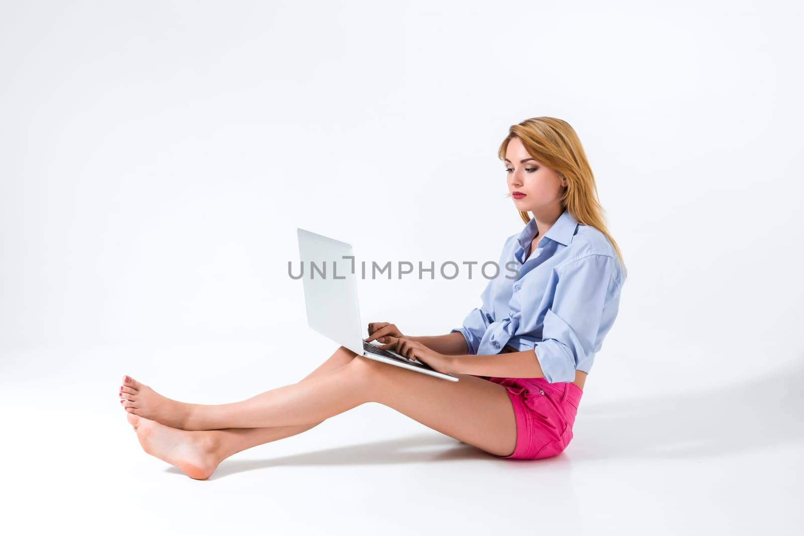 young woman sitting on the floor and using laptop on white background. satisfied, pleased, happy, smiling