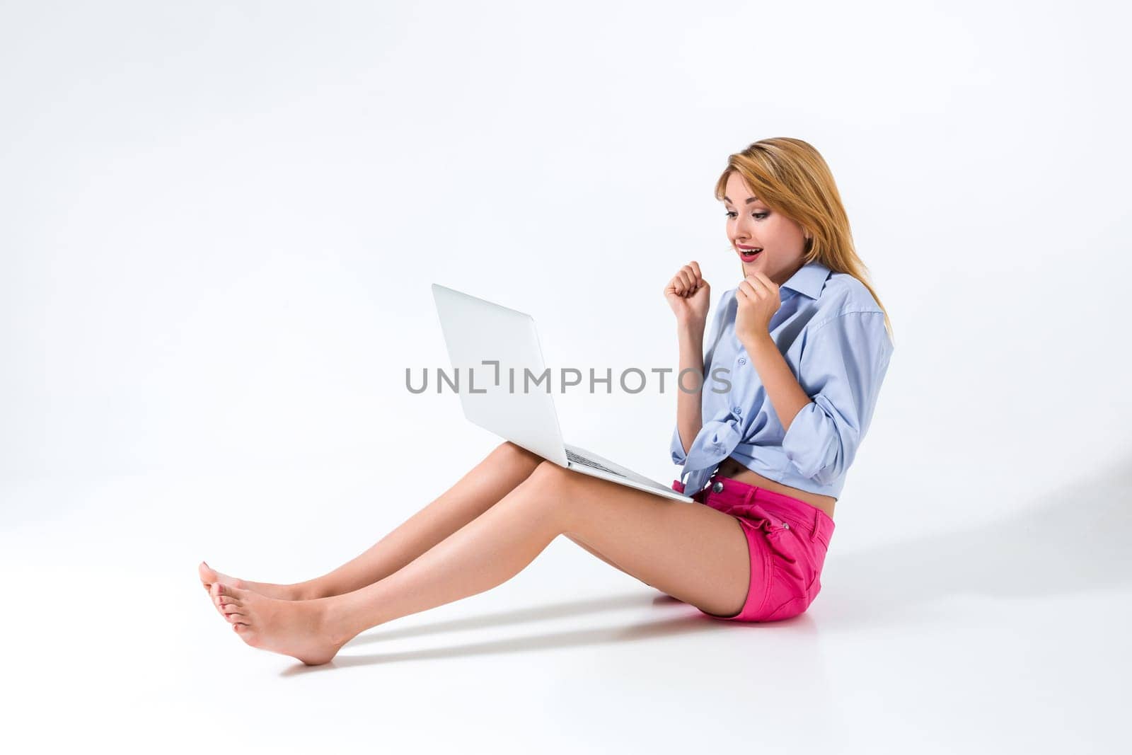 young woman sitting on the floor and using laptop on white background. Surprised, emotional