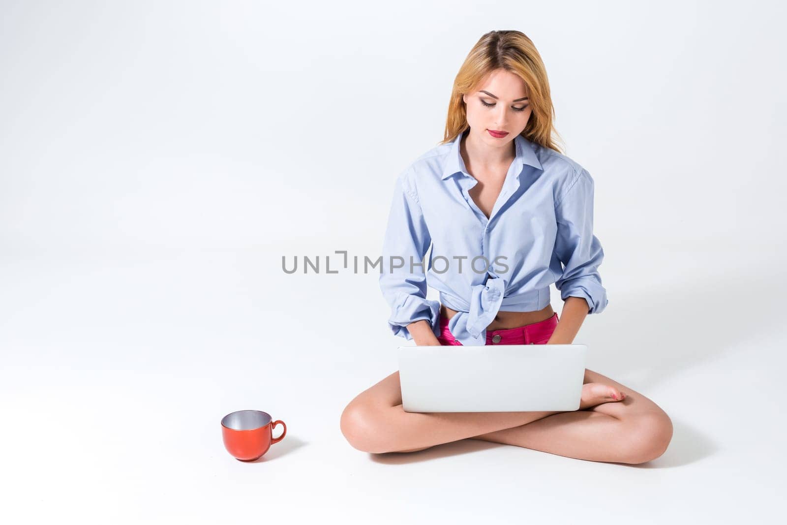 young woman sitting on the floor with crossed legs and using laptop on white background. typing on keyboard and looking at monitor