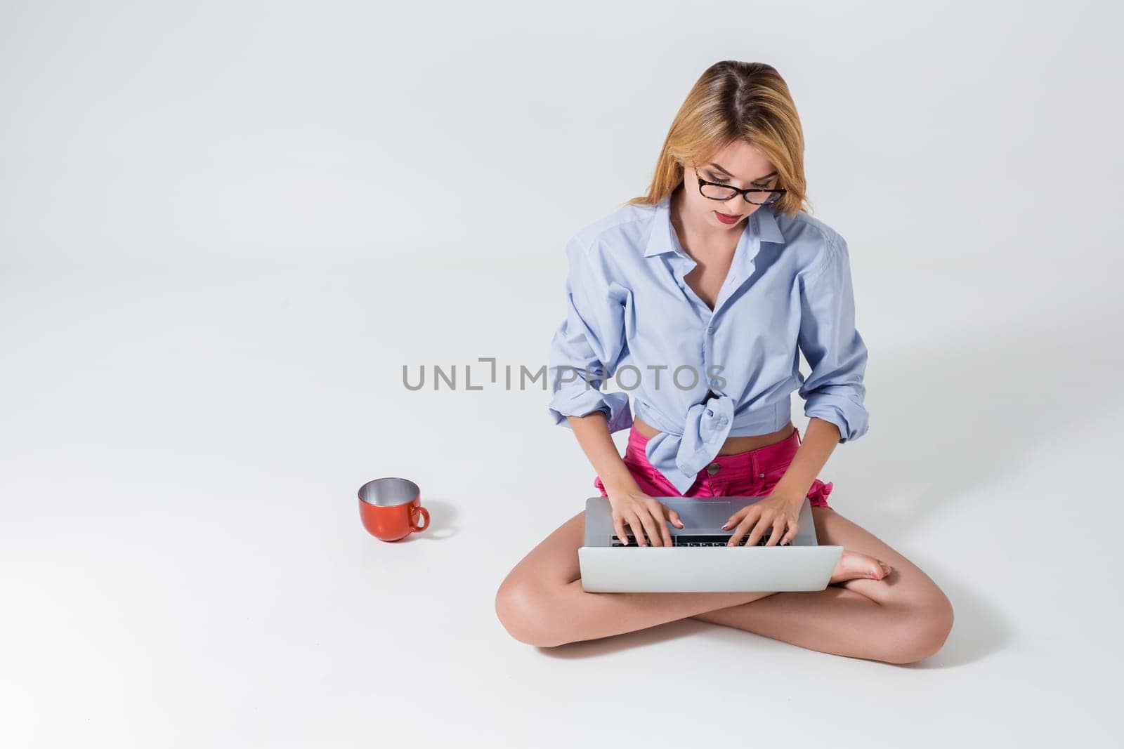 young woman sitting on the floor with crossed legs and using laptop on white background. typing on keyboard and looking at monitor