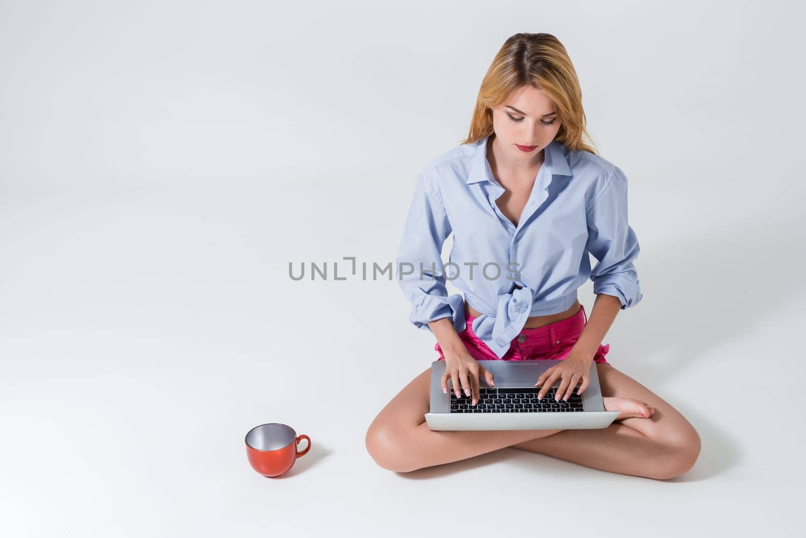 young woman sitting on the floor with crossed legs and using laptop on white background. typing on keyboard and looking at monitor