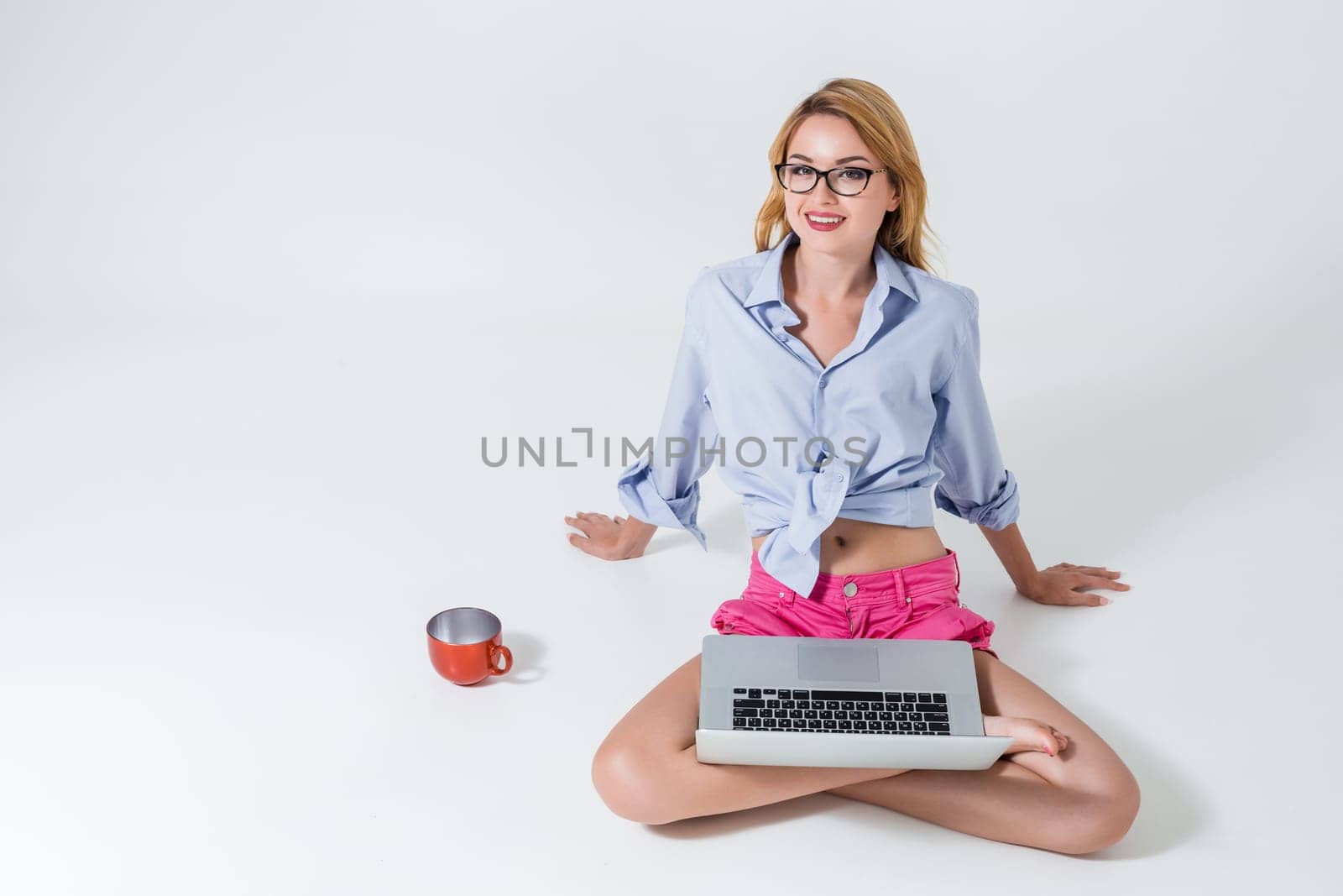 young woman sitting on the floor with crossed legs and using laptop on white background. satisfied, pleased, happy, smiling and looking at the camera