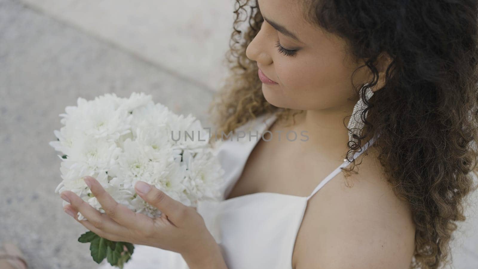 Beautiful young woman with bouquet of white flowers on street. Action. Attractive young woman smiles and holds bouquet of flowers. Smiling woman in dress and bouquet of flowers is waiting for date.