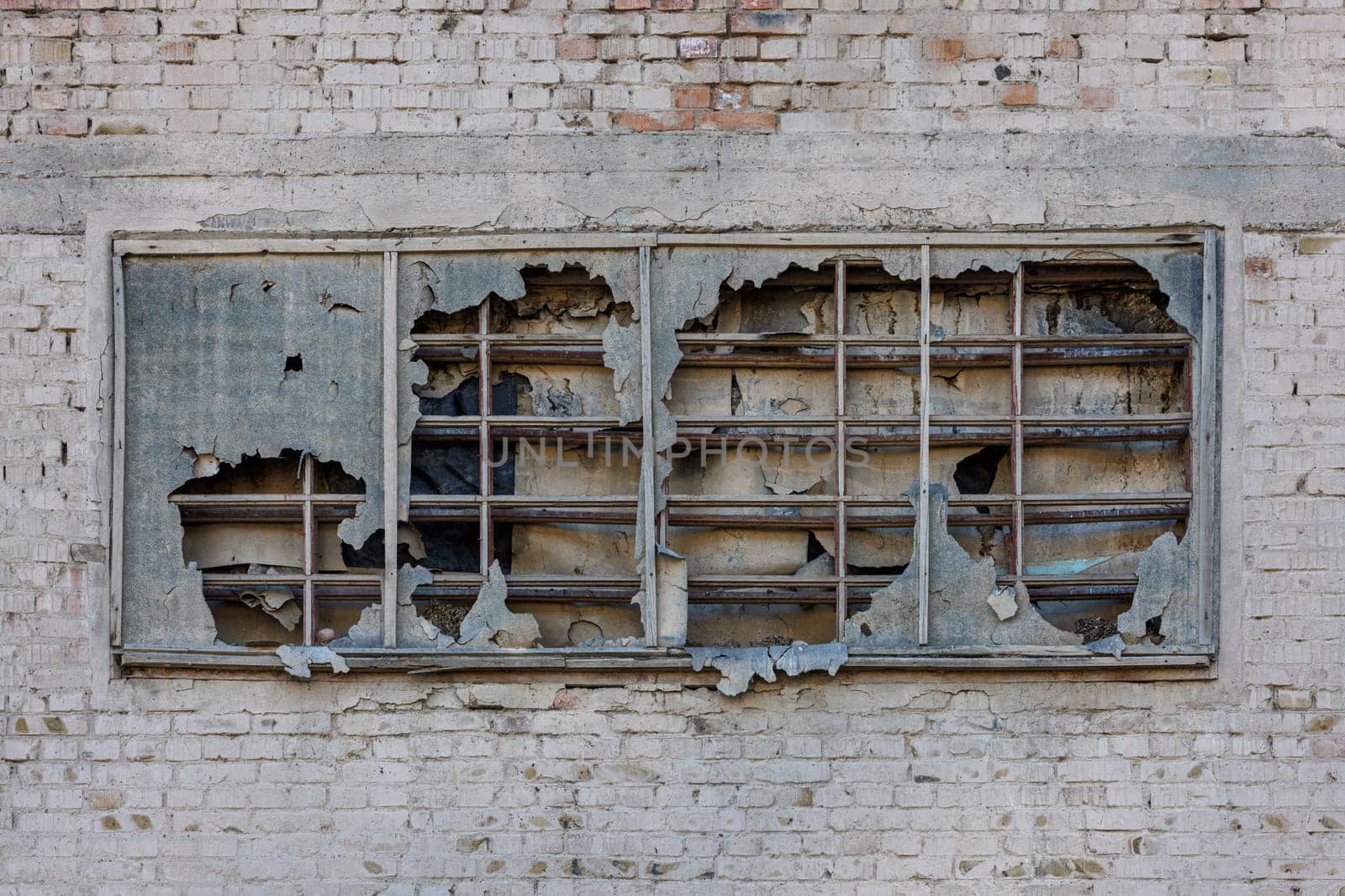 old window covered with torn ruberoid material and old wooden planks on white brick wall of an abandoned building, full-frame background and texture