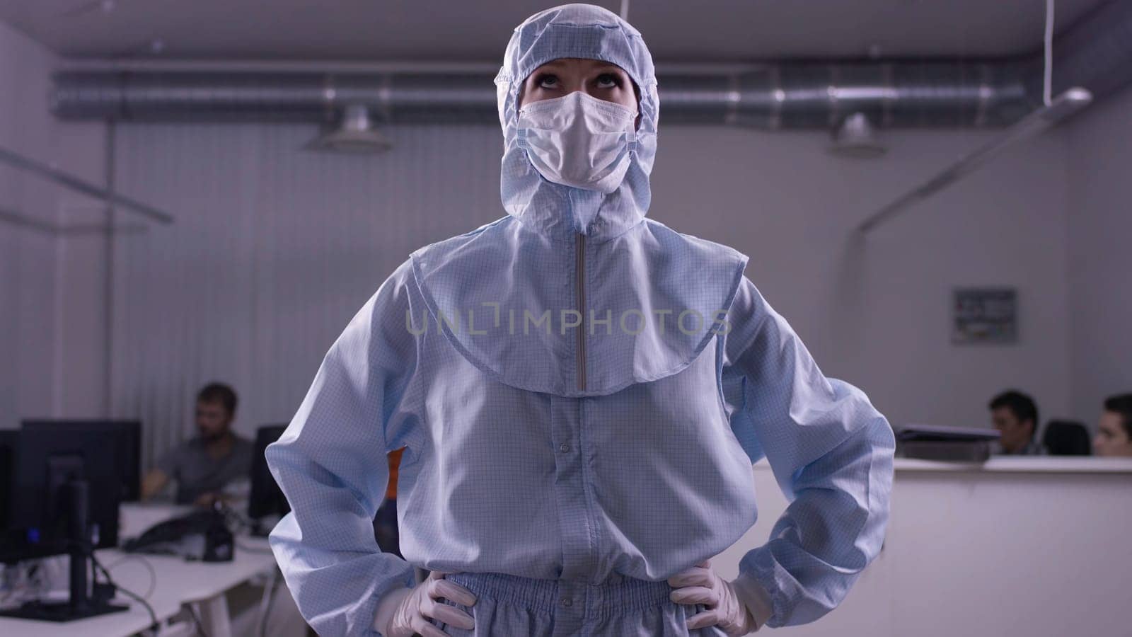 Woman standing in protective suit and looks around. Half-growth woman in white protective suit of synthetic paper and respiritory half mask, looking at us, hands in lock on chest