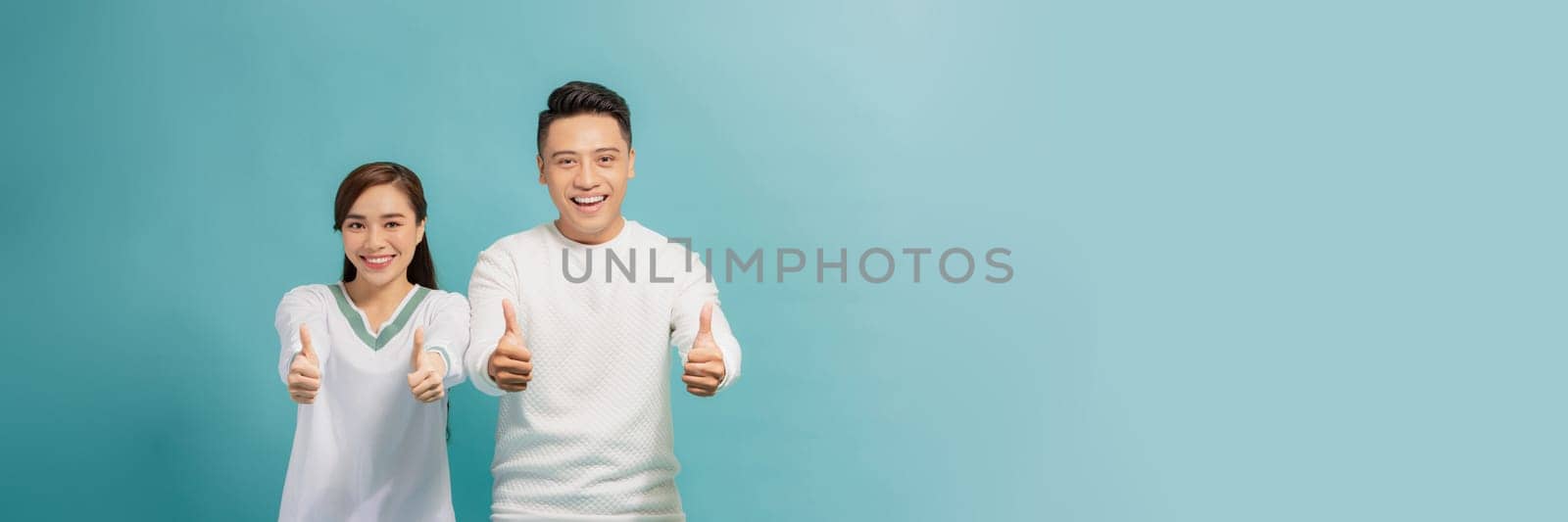 Charming positive husband wife cuddling showing you thumbs up isolated turquoise background by makidotvn