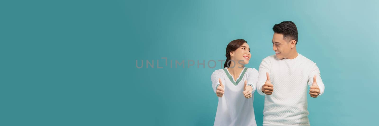 Photo of happy excited young loving couple standing isolated, showing thumbs up gesture.