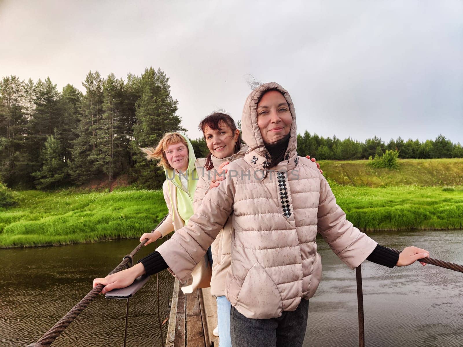 Three funny tourist girls on the old bridge in a cloudy summer or spring day. Middle-aged women having fun outdoors by keleny