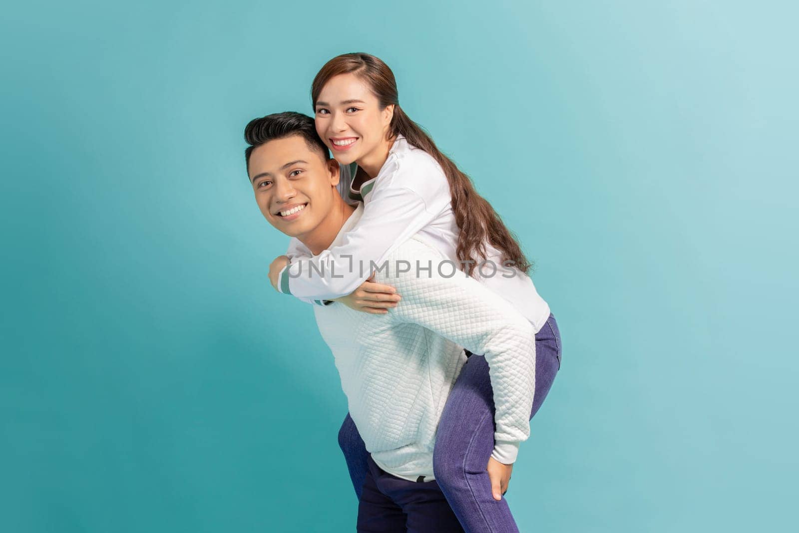 Happy smiling young asian couple piggyback isolated on light blue background by makidotvn