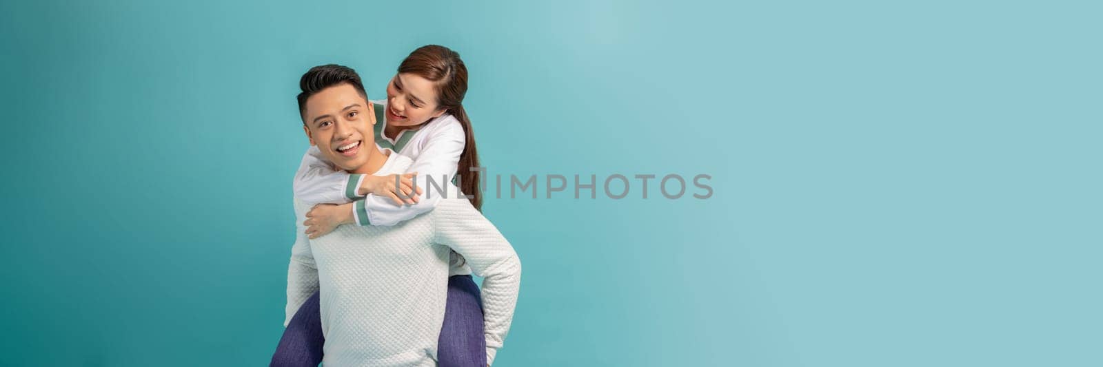 Happy smiling young asian couple piggyback isolated on light blue background by makidotvn