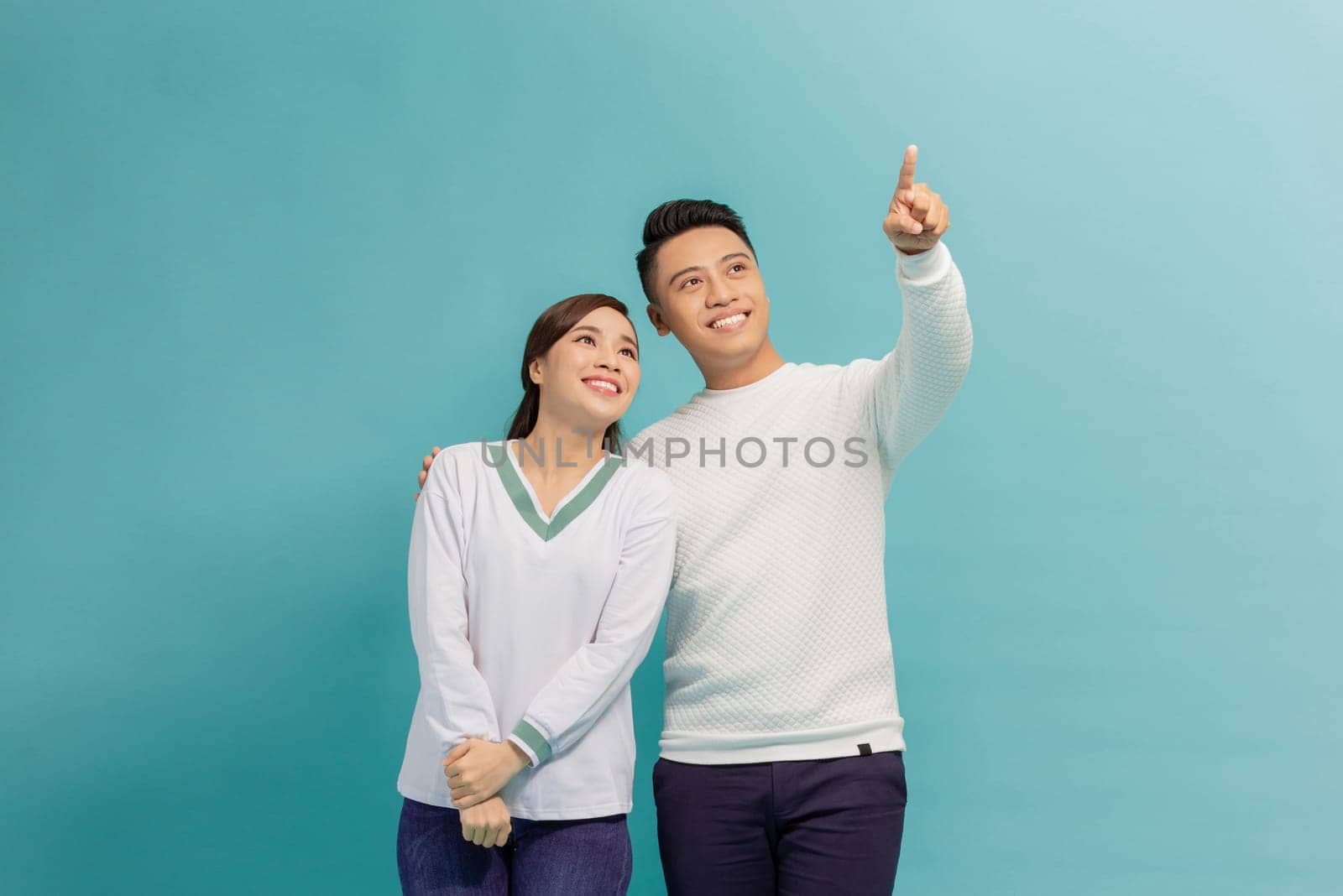 Young couple together with a big smile on face, pointing with hand finger to the side by makidotvn
