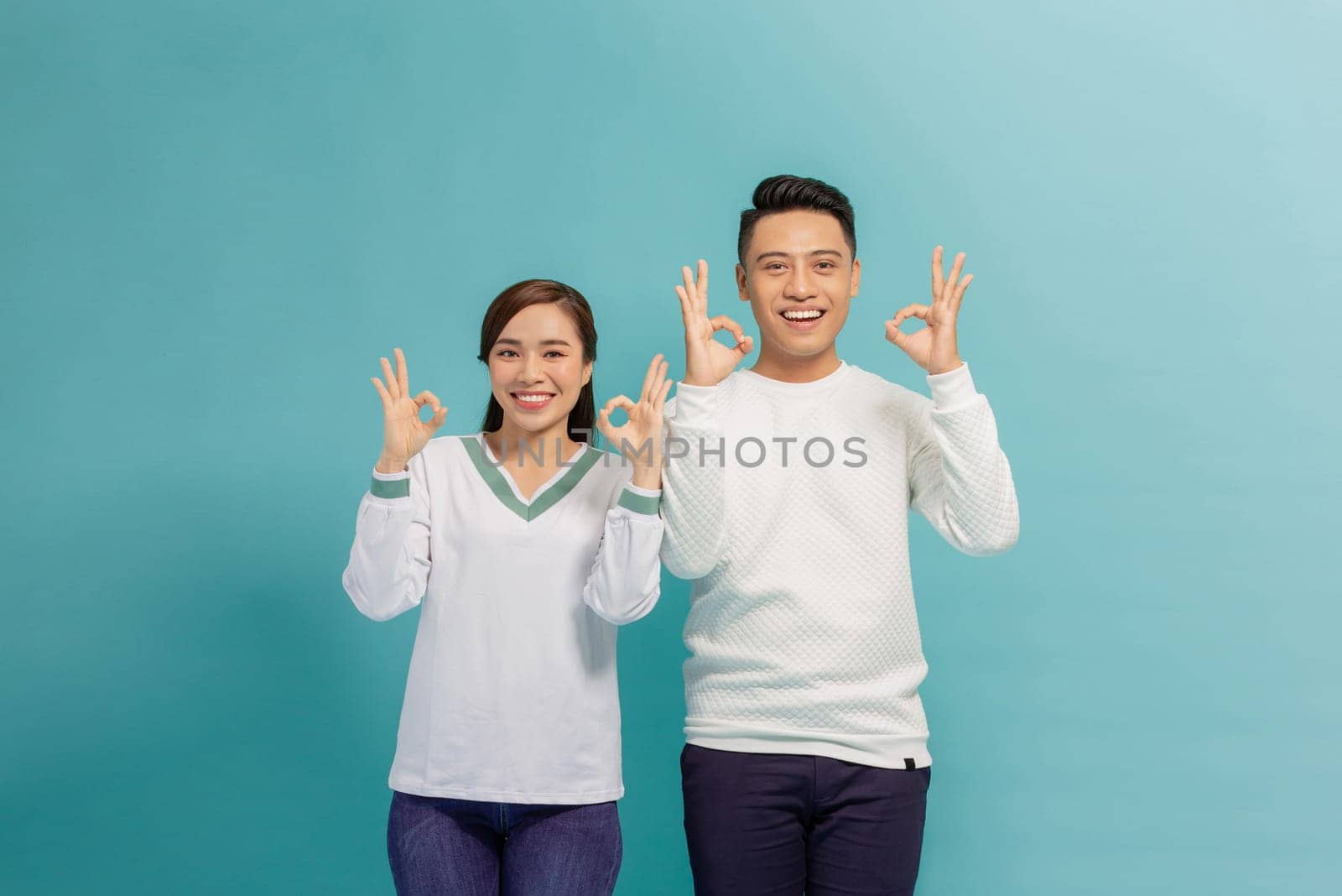 Portrait of young Asian couple showing ok sign isolated on  blue background, Two people concept