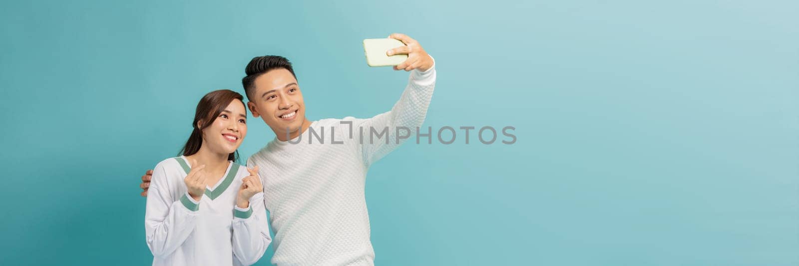 Smiling asian couple having fun together while making selfie on smartphone over blue background