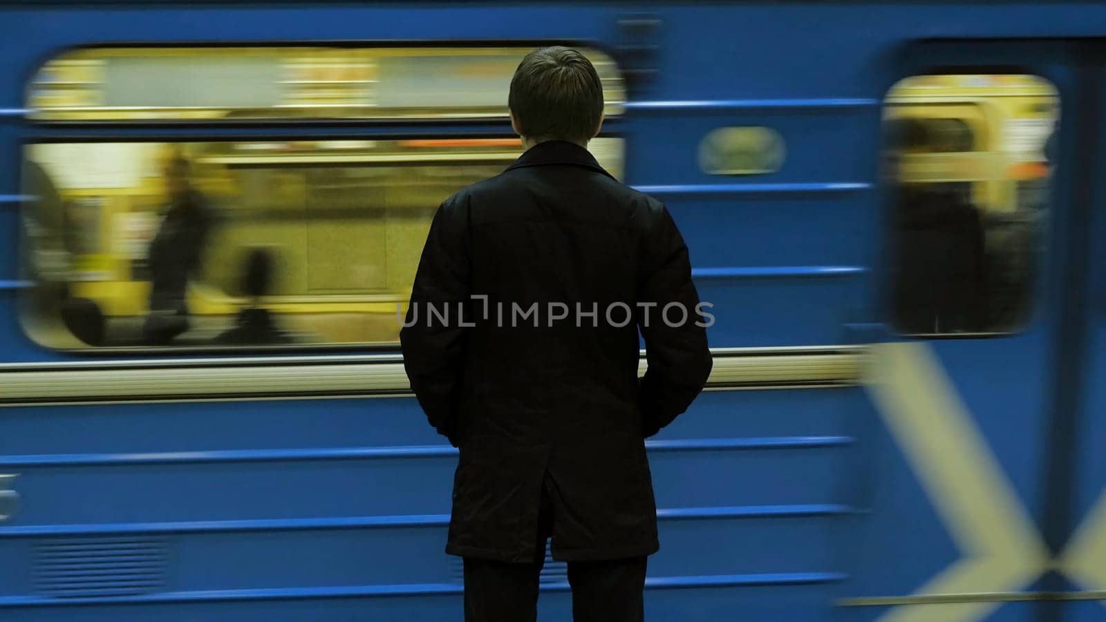 Lonely young man from behind at subway station. Young man waits for a train in the subway, rear view.