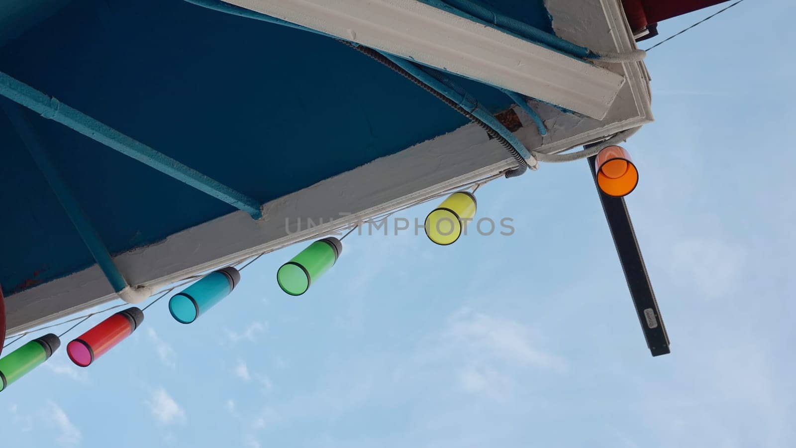 Colorful lanterns on roof. Action. Multicolored glass light bulbs hang from roof of house. Beautiful colorful lights on blue sky background.