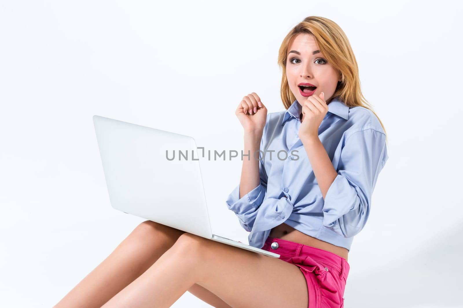 young woman sitting on the floor and using laptop on white background. Surprised, emotional