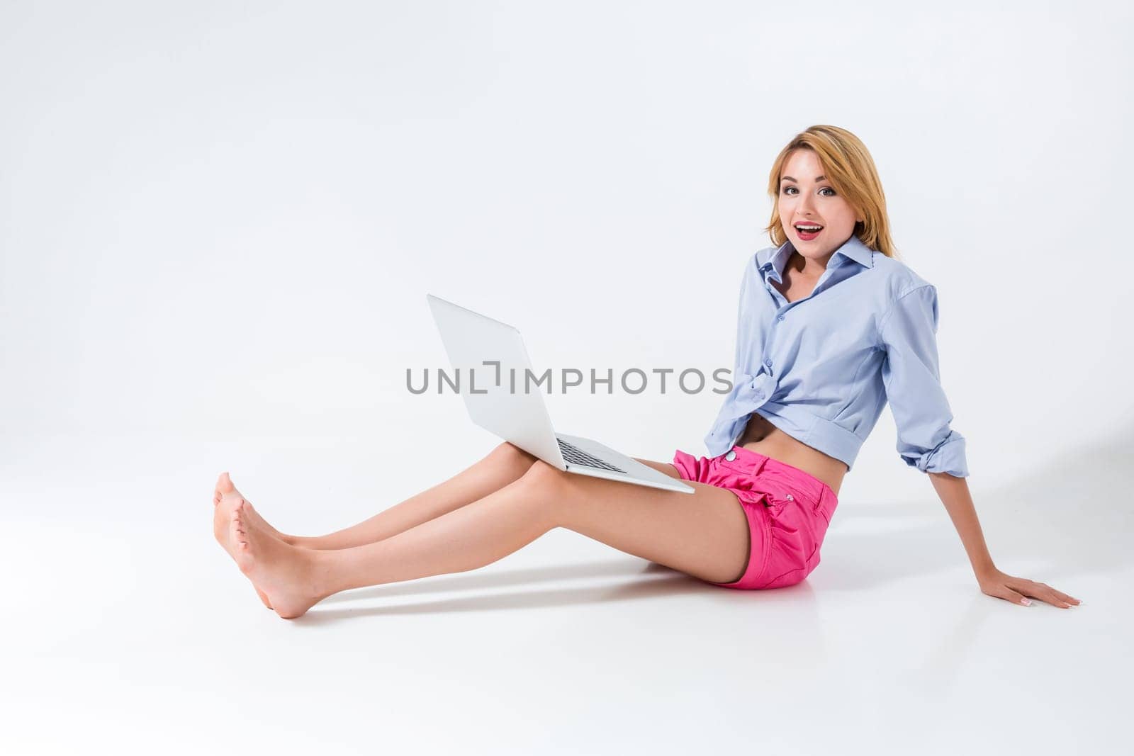 young woman sitting on the floor and using laptop on white background. satisfied, pleased, happy, smiling