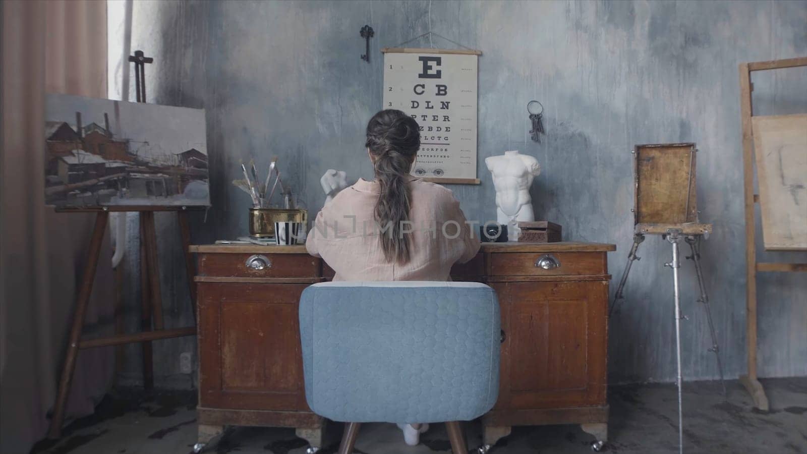Businesswoman typing something on laptop and sitting at the desk, rear view. Back view of brunette woman sitting in the art workshop.