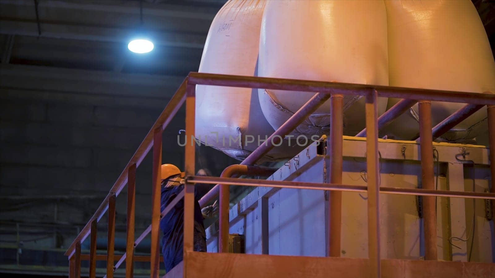 Worker at factory with bags for raw materials. Stock footage. Worker in hard hat opens suspended bags filled with raw materials for mixing in industrial equipment.