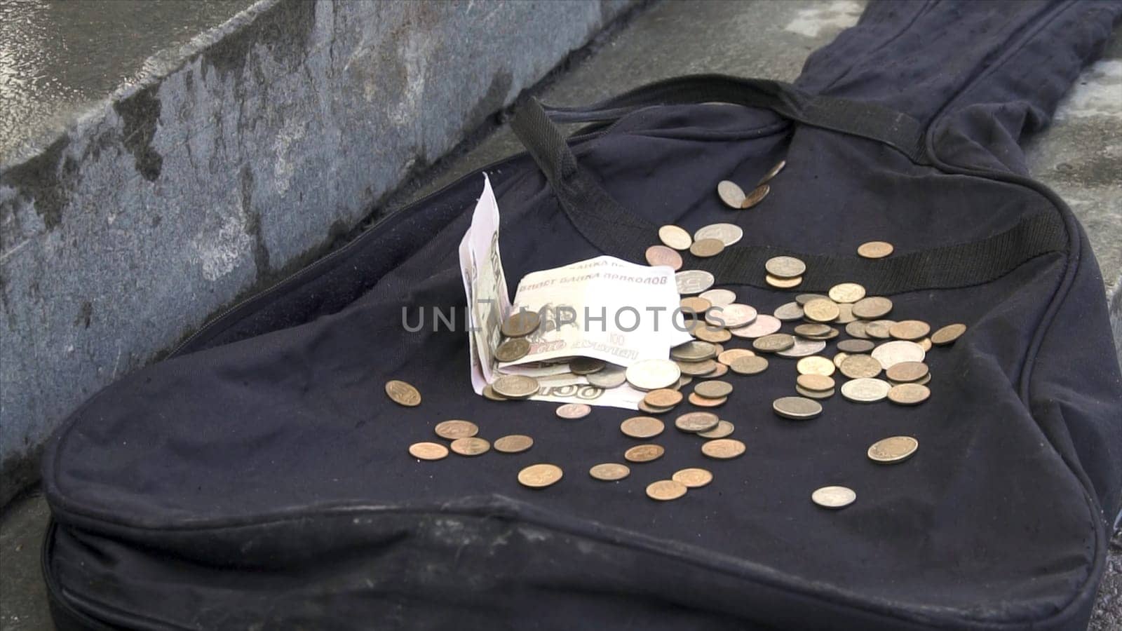 Russian rubles falling on black guitar case on outdoor city sidewalk. Close up for paper money and coins lying on black, empty guitar case, poverty concept
