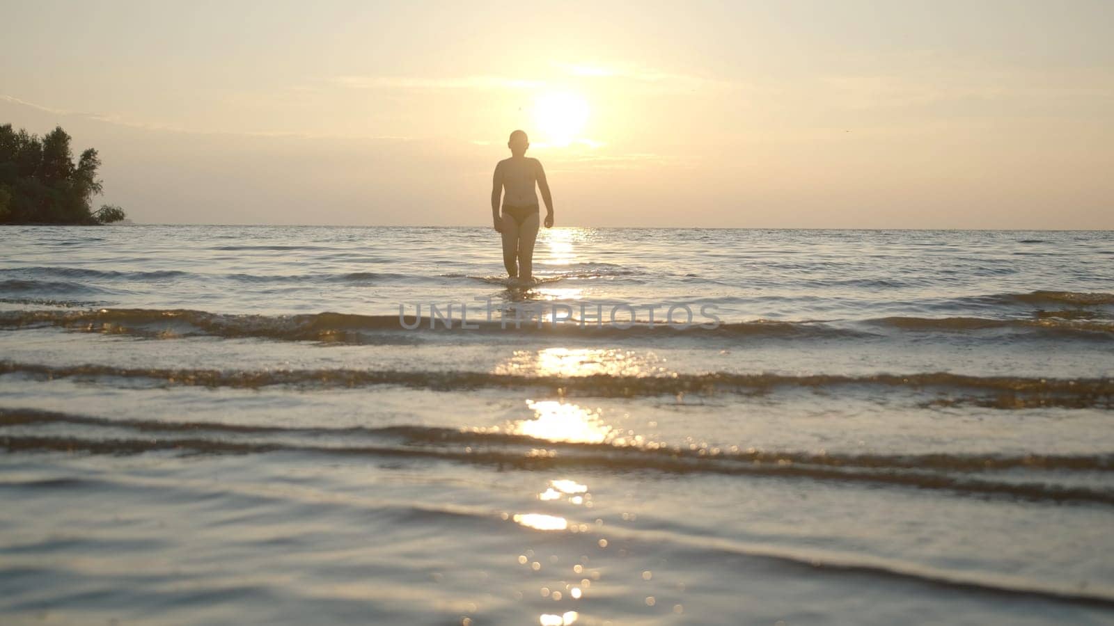 Silhouette of man walking in water on sunset background. Creative. Man comes out of water on background of sunset. Man comes out of water at sunset.