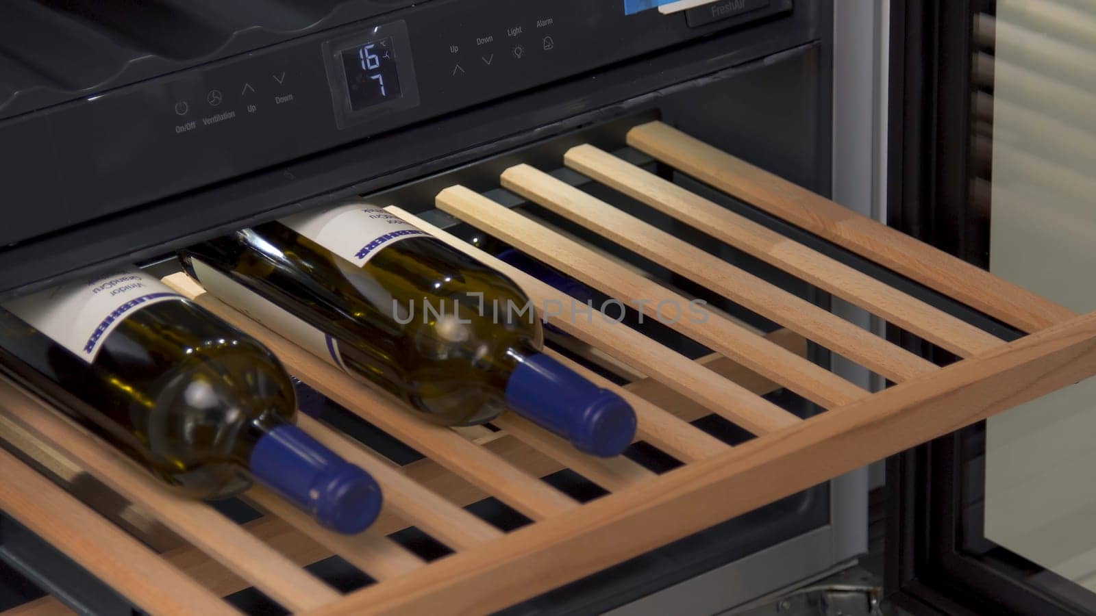 Storing bottles of wine in fridge for cooling and preserving wine. Close up of man demonstrating home use wine cooler at the shop of home appliances.