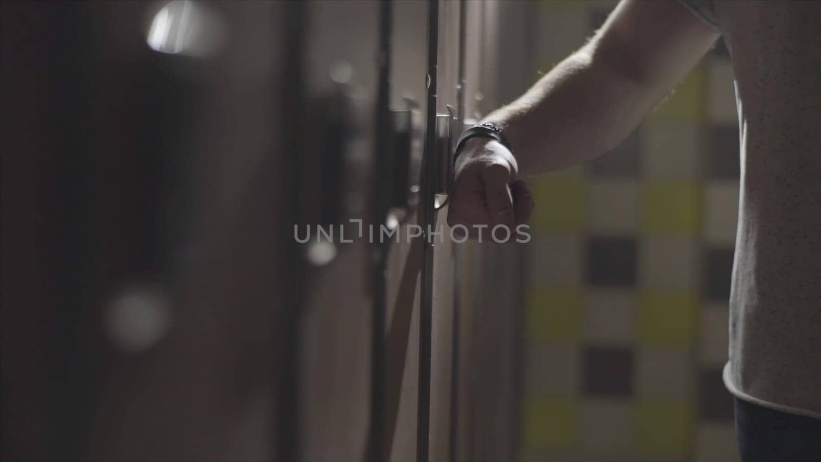 Man's hand opening locker with electric key on his wrist at gym in the changing room. Close up hand opening the locker door in the changing room of a gym.