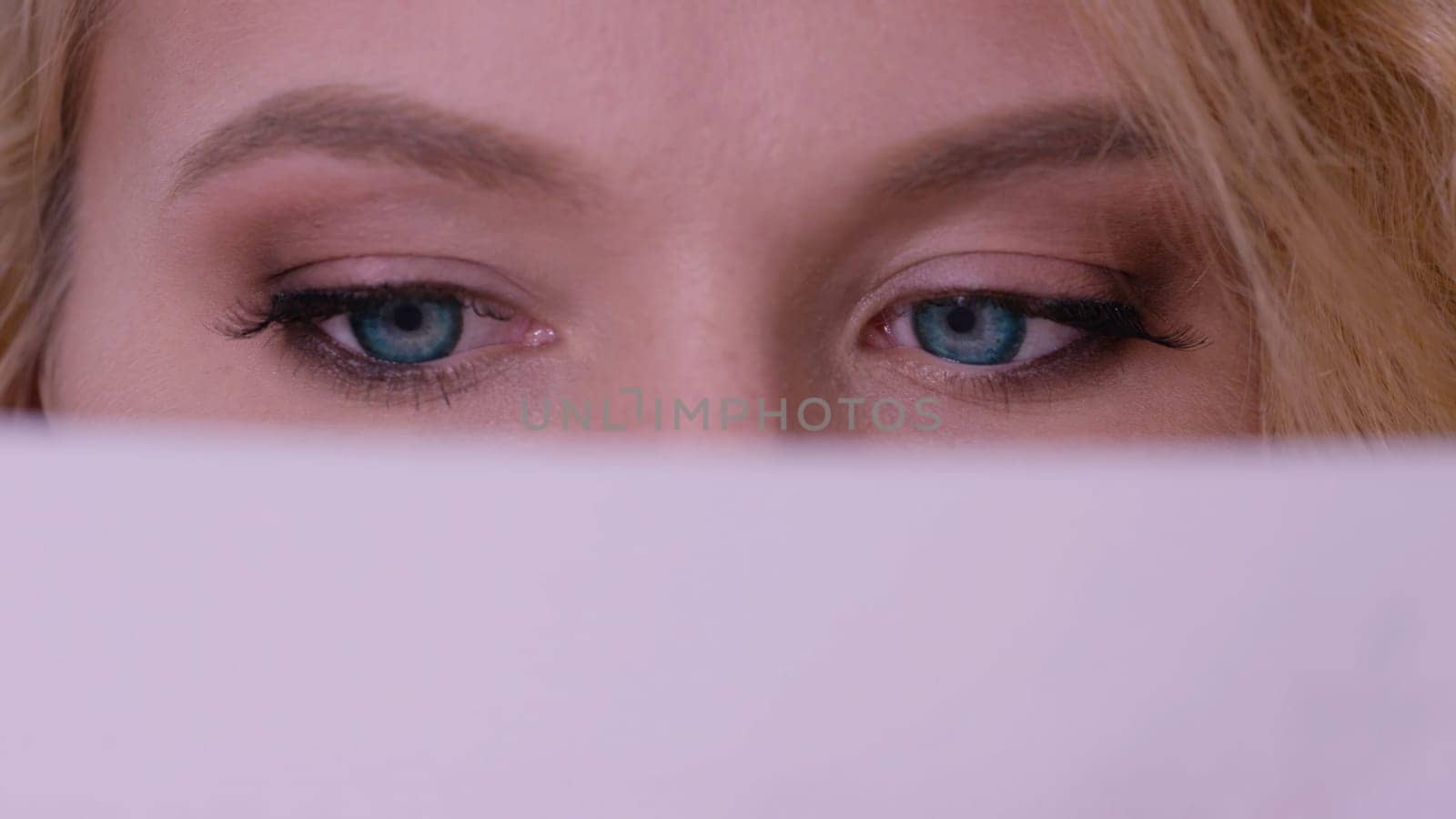 Closeup of woman face behind book cover. Close up of redhead girl with blue eyes behind book. Learning and reading concept. Women's eyes read close up.