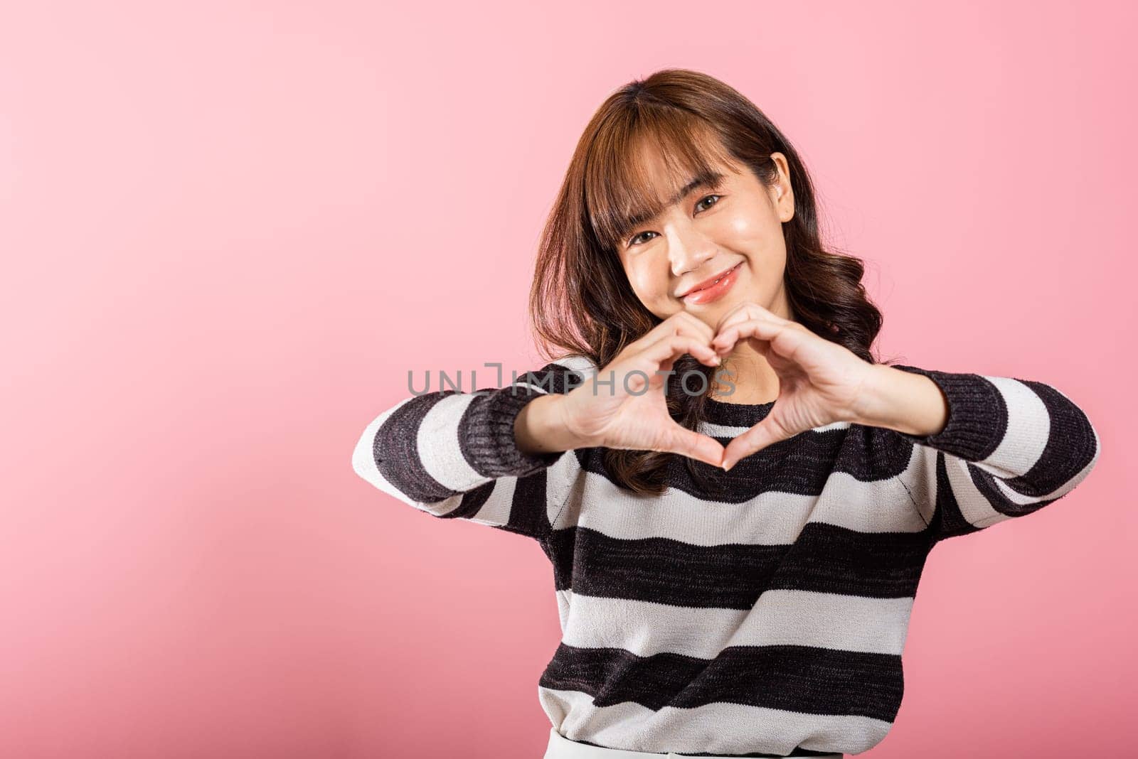 Portrait of a happy Asian lady with a confident smile, making a heart symbol with her fingers and hands by Sorapop