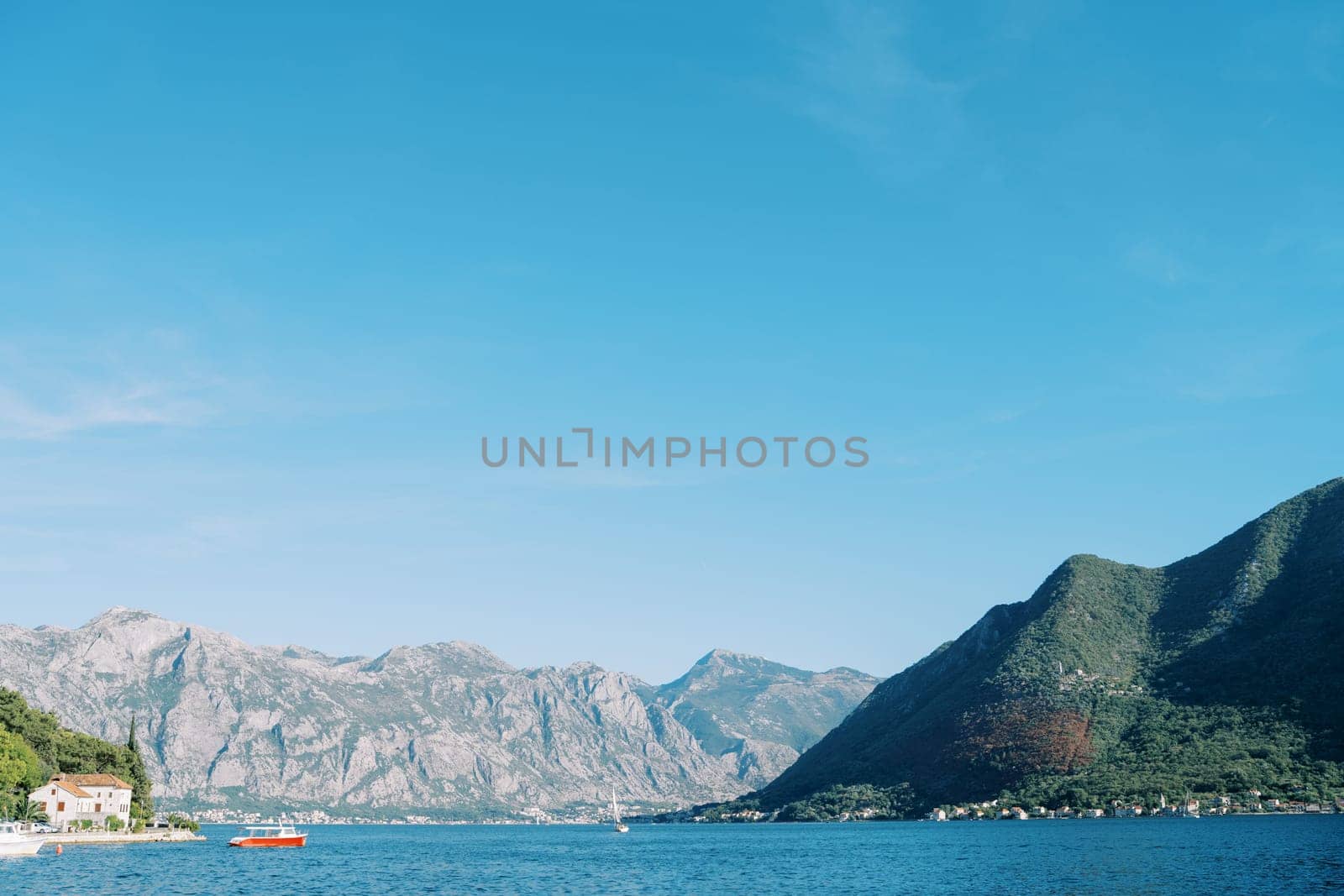 Red motorboat sails on a bay near a mountainous coast by Nadtochiy