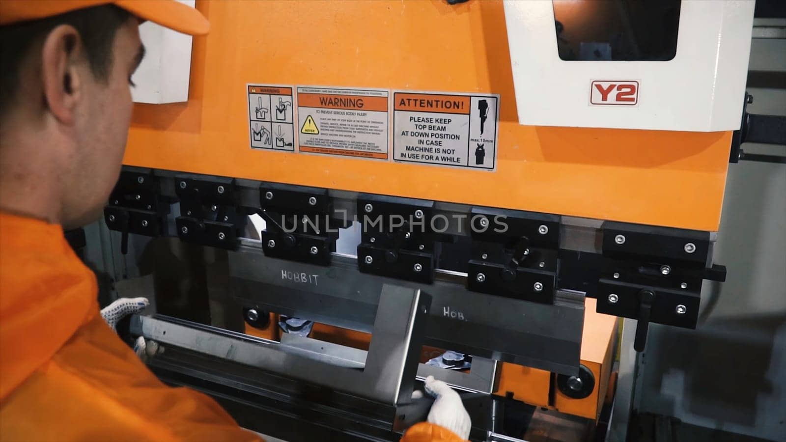 Worker in factory at metal skip machine putting work piece in. Clip. Man working with sheet metal and special machine tools for bending.