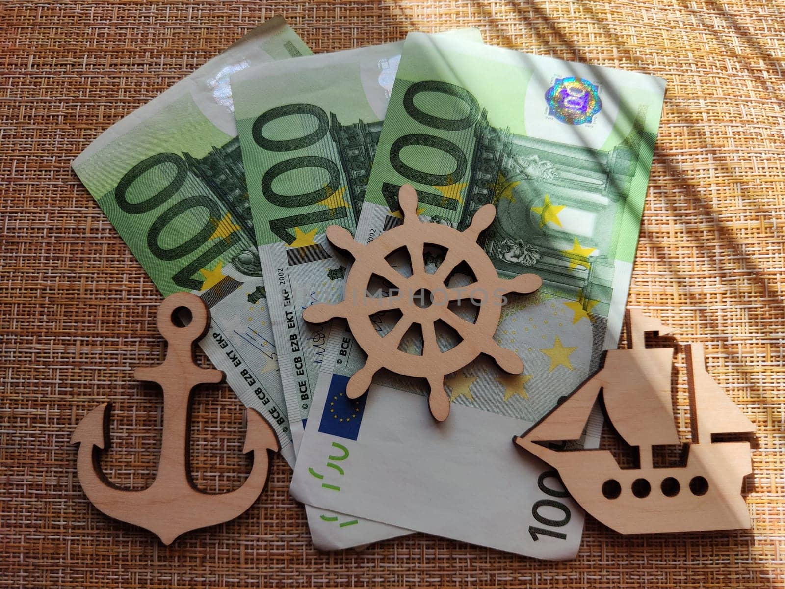 Euro paper money and wooden figurines with a ship, a lighthouse, and a steering wheel. The concept of travel and its cost. The expensive price of a trip to the sea. Sailing by keleny