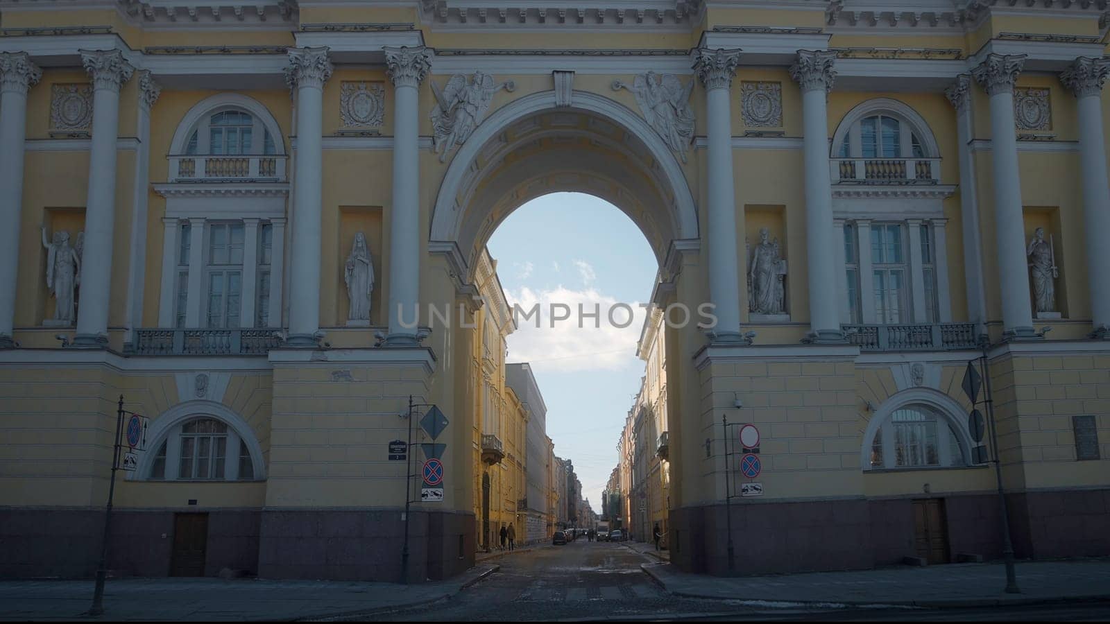 Beautiful view of street through ancient arch. Action. Ancient architectural arch overlooking street on sunny day. People walk along street with old arch.