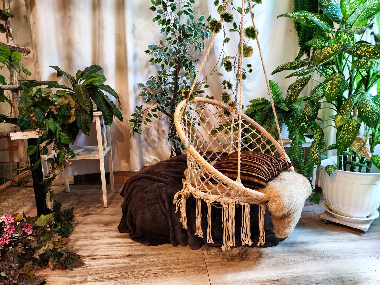Modern cozy beautiful room with a braided rope macrame chair, green plants and a window with curtains. Interior and background. Location for photo shooting