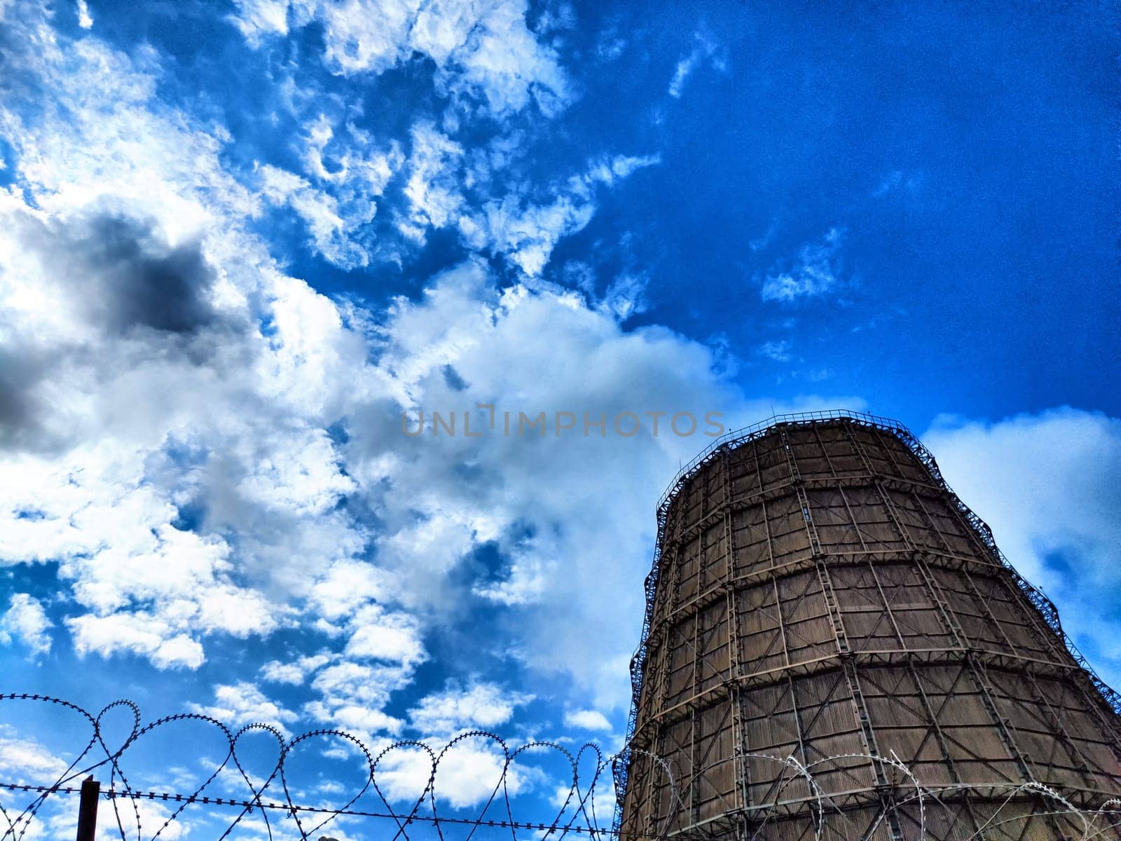 Big tower of CHPP close-up. White steam from wide pipe of CHP and blue sky. Industrial background. Huge pipes of thermal power plant produce steam for electric power. Strategically important object