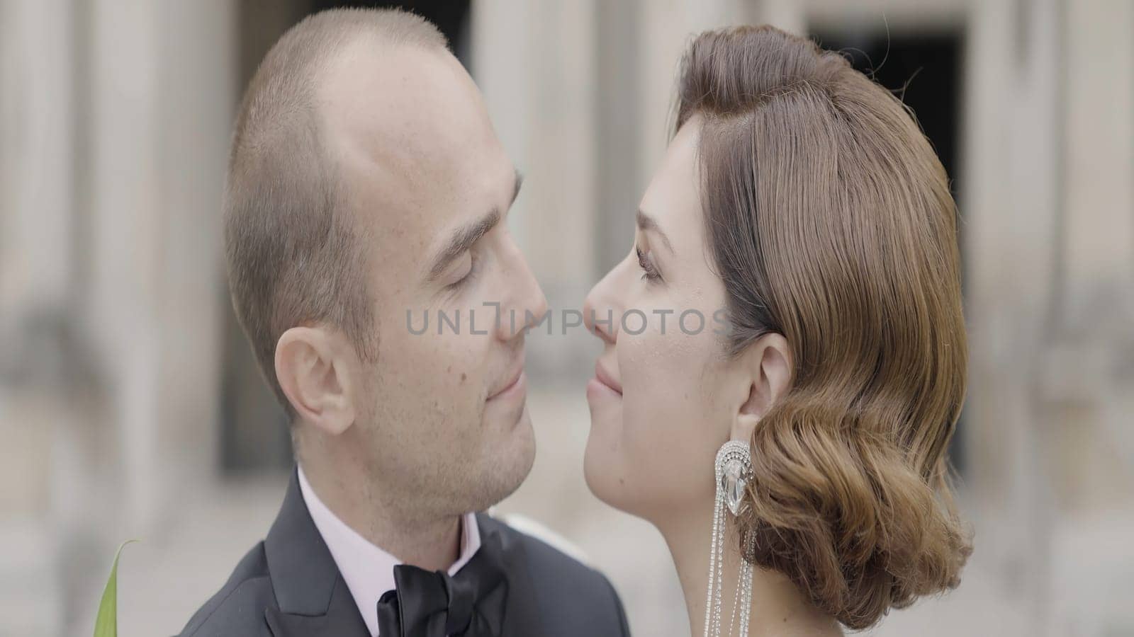 Close up of lovely couple together in slow motion outdoors. Action. Romantic couple hugging, wearing suit and white dress with long attractive earring