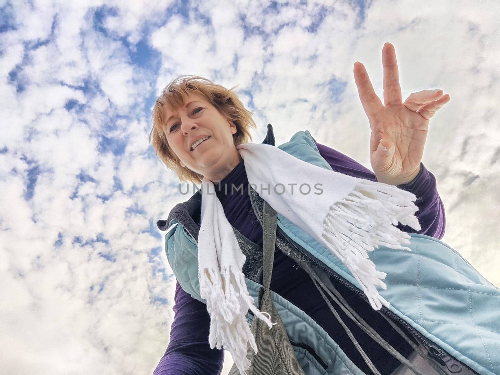 A happy, funny, funny adult girl takes a selfie against a blue sky with white clouds. A middle-aged woman poses on the phone in nature in autumn or spring by keleny