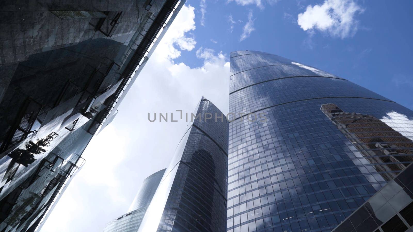 Bottom view of glass skyscrapers on background blue sky. Action. Dizzying view of business high-rise in center of modern city. Glass skyscrapers reflect blue sky.